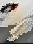 Porcelain Doll in White Bridal Dress with Veil: This porcelain doll has curly brown hair, a gentle smile, and brown eyes. She is dressed in a satin-like white dress with lace bodice detailing and puffed sleeves, finished with a ribbon flower at the