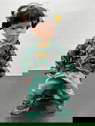 Porcelain Doll in Traditional Chinese Outfit: This porcelain doll features black hair styled in traditional buns with yellow floral accents and a gentle, thoughtful expression. She is dressed in a beautiful emerald green silk-like outfit with