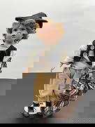 Porcelain Boy Doll in Newsboy Outfit with Plaid Blanket: This porcelain boy doll features curly blonde hair, soft facial features, and a slightly open-mouthed expression. He is dressed in a vintage-inspired outfit consisting of a cream knit shirt, black