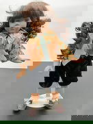 Porcelain Doll in Sunflower Shirt and Velvet Shorts: This porcelain doll features long dark curly hair tied in pigtails and warm brown eyes. She is dressed in a sunflower-patterned blouse with a burnt orange textured vest and a forest green tie. Her