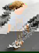 Porcelain Doll in Striped Overalls with Pigtails: This porcelain doll has light brown hair styled in playful pigtails tied with red and green hair ties. She wears a casual outfit featuring blue and multicolored striped overalls with a denim chest