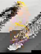 Porcelain Doll in Purple Floral Dress with Sun Hat: This porcelain doll has long curly brown hair and bright green eyes with a soft expression. She is dressed in a cheerful springtime outfit featuring a white dress with floral and purple cross