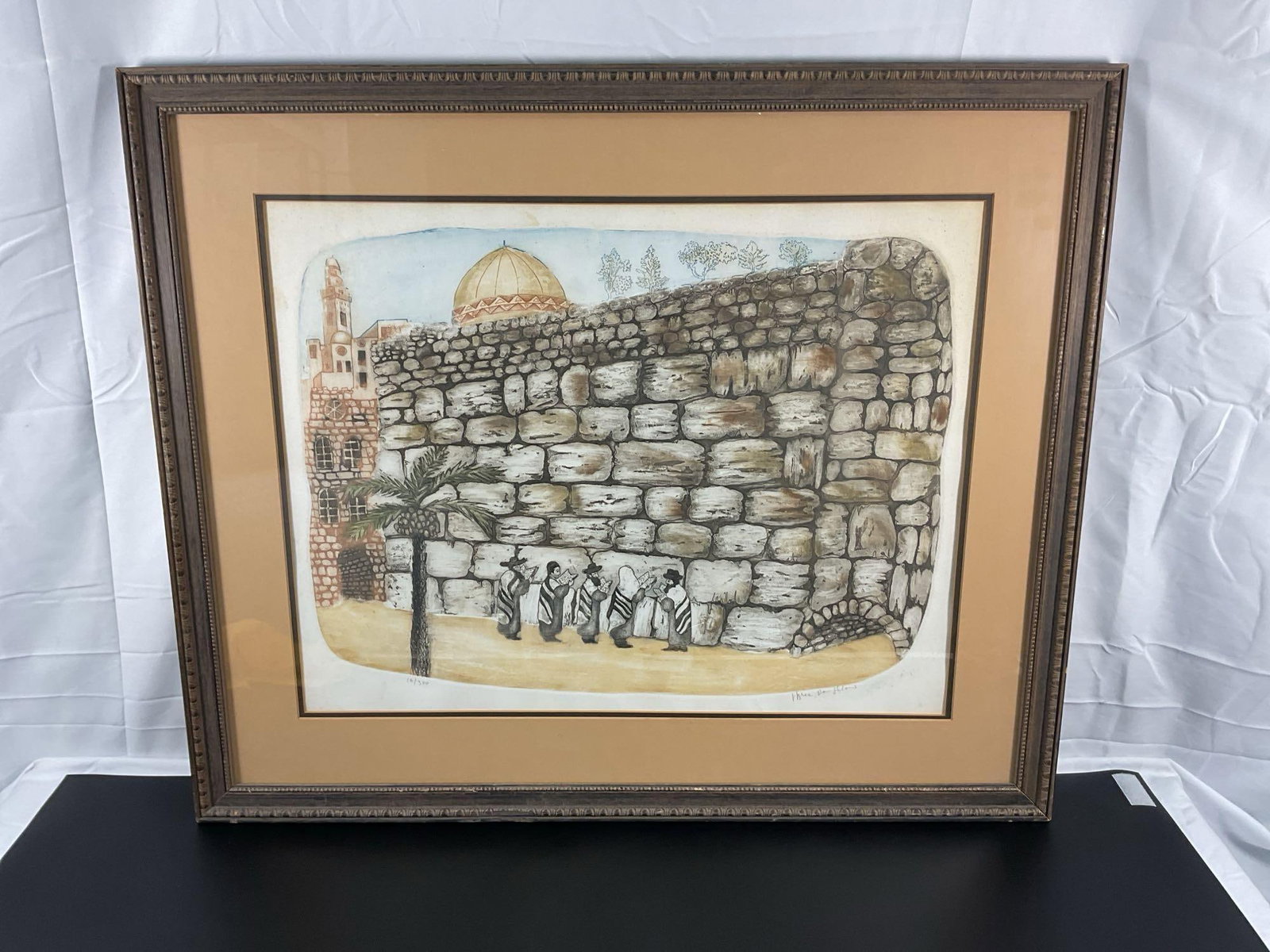 Shemtov Ben Shlomo (Israeli) Lithograph: This framed artwork depicts a scene of the Western Wall (Wailing Wall) in Jerusalem, featuring figures in traditional attire praying at the base of the ancient stone wall. The composition includes