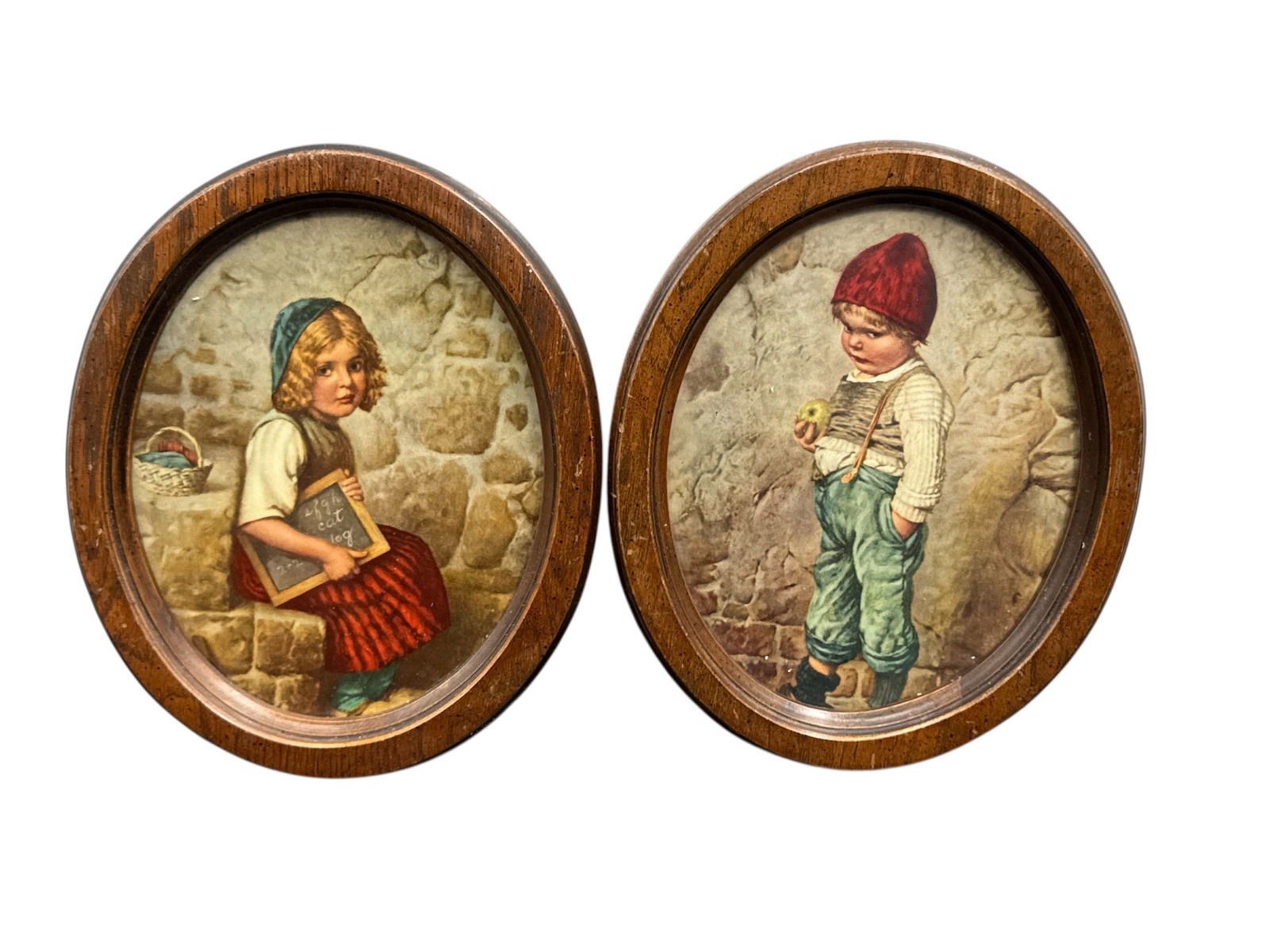Pair of Oval Framed Child Portrait Prints: Charming pair of oval framed prints depicting a young girl and a young boy in rustic attire, each shown against a stone wall setting. The images feature soft, warm tones and nostalgic subject matter