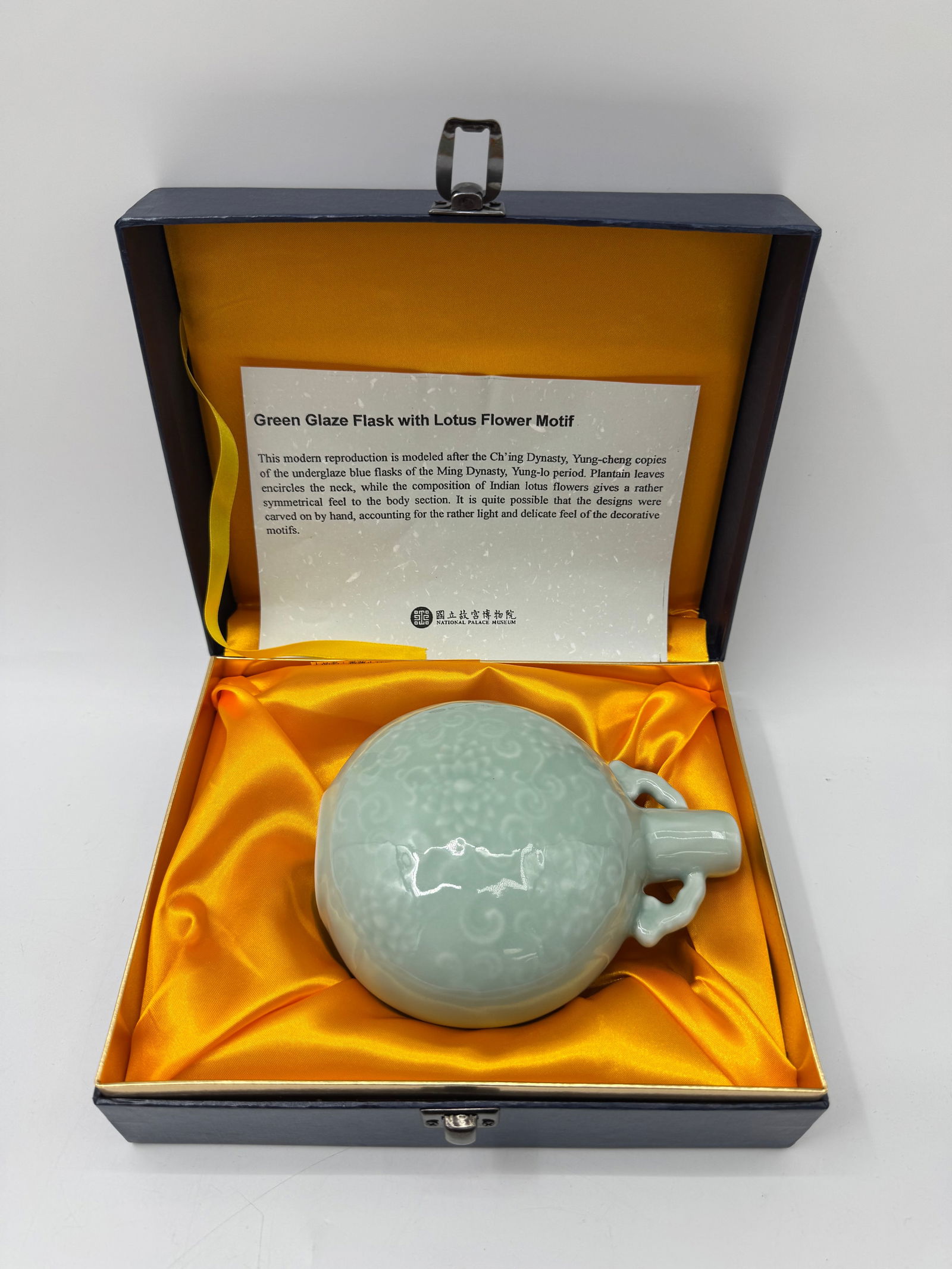 Green Glass Flask with Lotus Flower Motif in Box: Green glass flask with lotus flower motif. Includes a fitted presentation box with silk lining and descriptive card. Flask measures approximately 6 x 5 inches; box measures 9 x 7.5 inches.