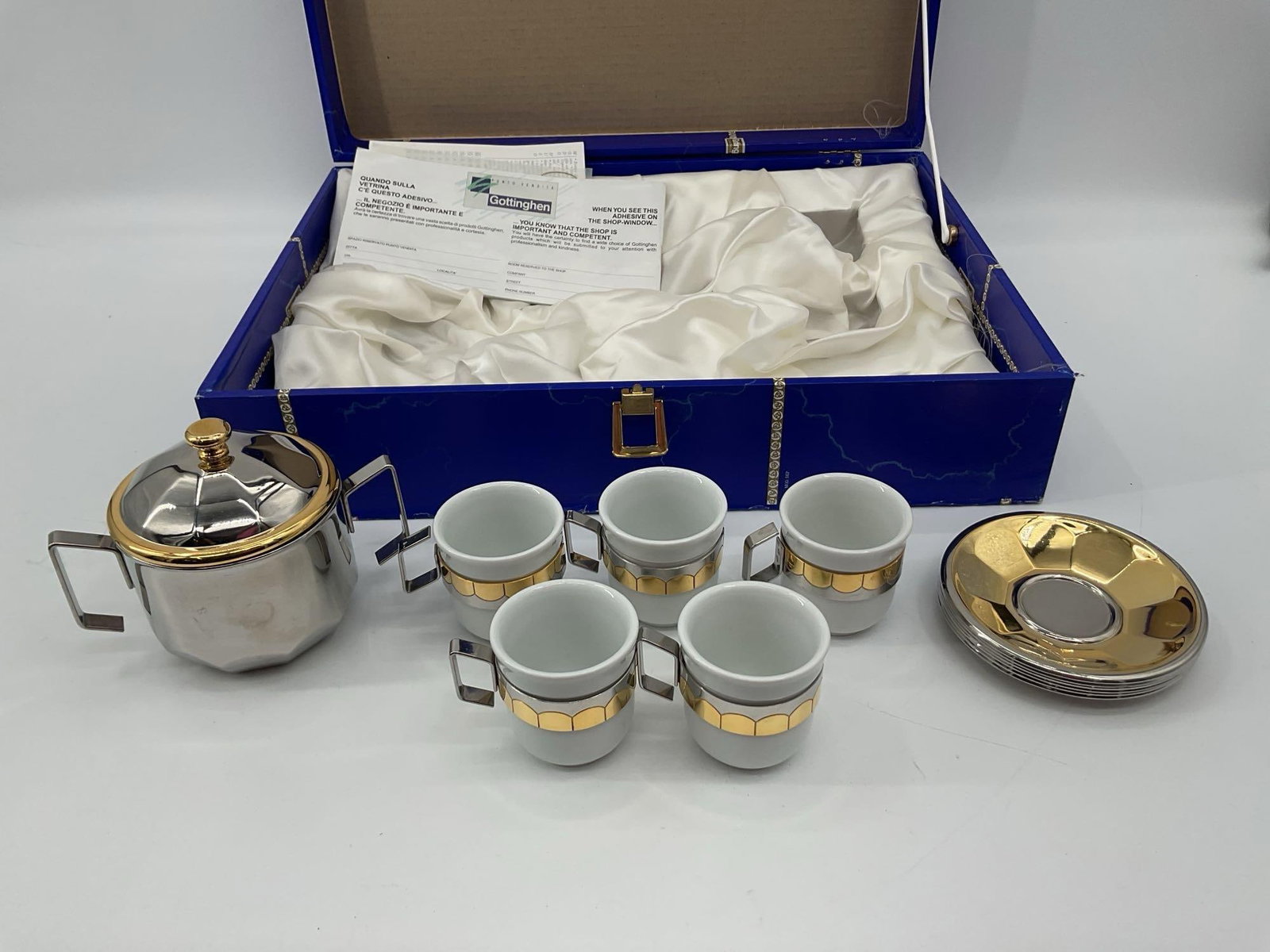 Oro Zecchino Espresso Set in Presentation Case: Elegant espresso set by Oro Zecchino featuring five white porcelain demitasse cups with bold metallic gold and silver-toned holders and saucers. Set includes a matching lidded sugar bowl, all housed
