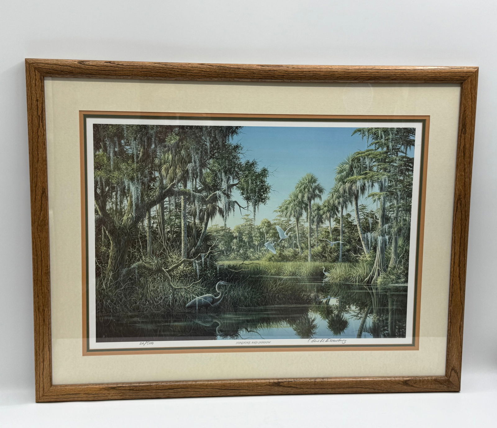 Framed Print by Ben W. Essenberg, "Sunshine and Shadow": Framed print by Ben W. Essenberg titled "Sunshine and Shadow". The print depicts a serene swamp scene with a heron in the water. It is numbered 26/500 and signed by the artist. The print is