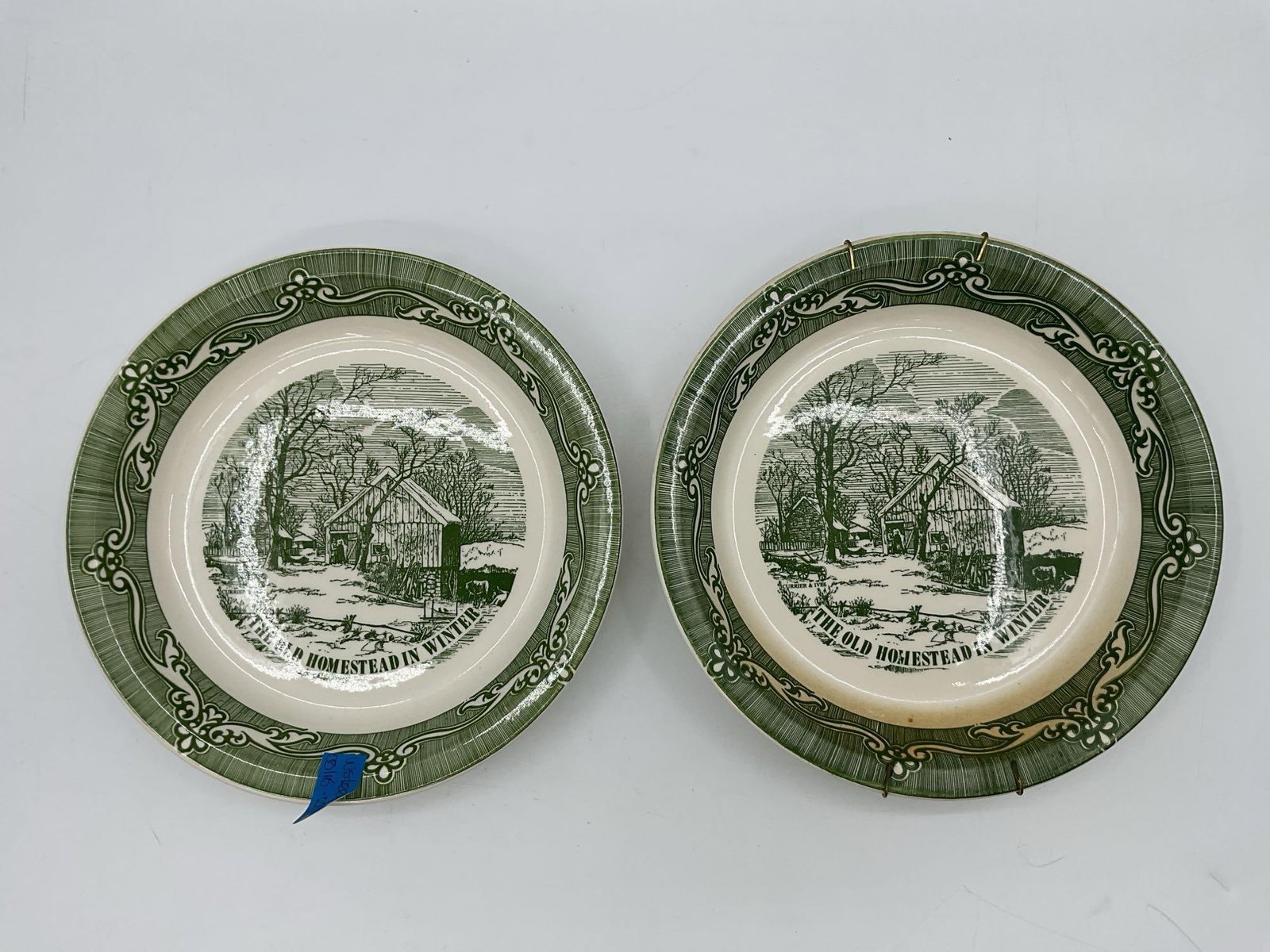 The Old Homestead in Winter by Currier and Ives: Pair of green transferware plates featuring a winter farm scene, based on the classic Currier and Ives lithograph, with decorative borders and historical notes on reverse Dimensions: diameter 10in Med
