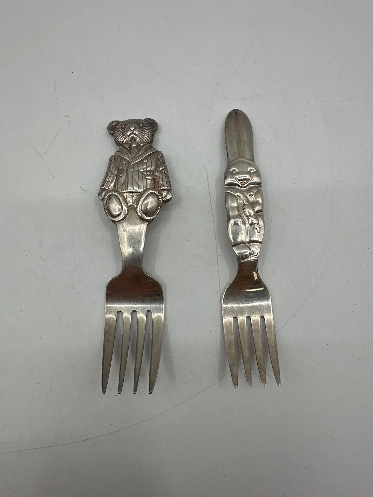 Pair of Vintage Children's Character Forks – Bunny and Teddy Bear - Reed & Barton and Ralph Lauren: Set of two silver-tone children's forks featuring whimsical character handles. One handle is shaped like a cheerful bunny, and the other depicts a teddy bear in a sailor outfit. Likely mid-20th
