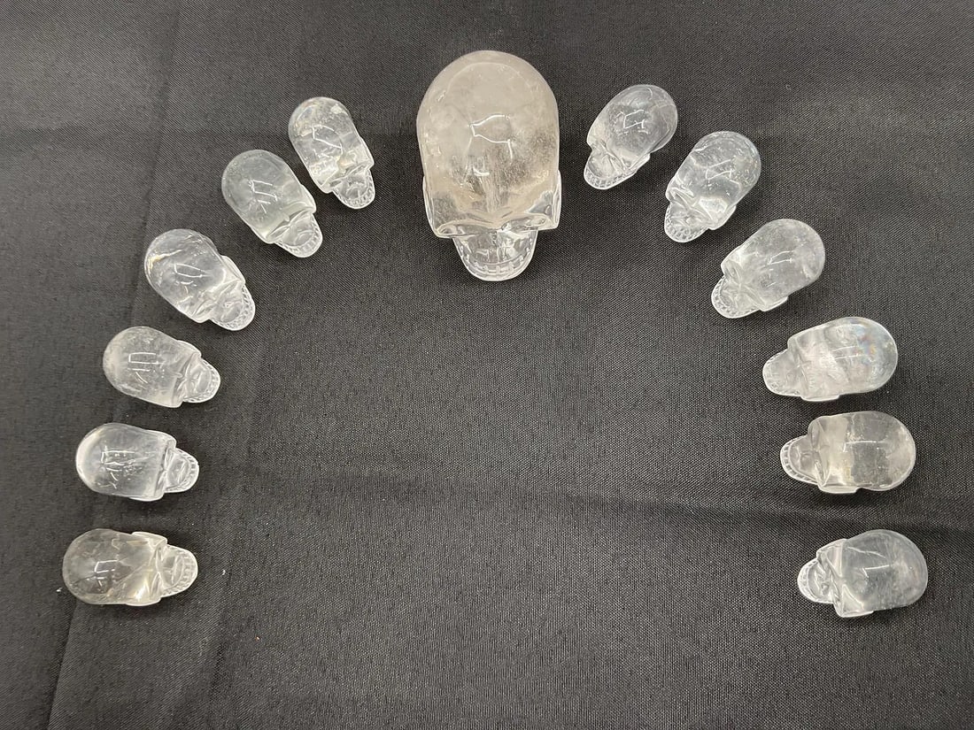 Set of Clear Tibetan Quartz Crystal Skulls with Informational Pamphlet: Boxed set featuring a large central clear quartz skull surrounded by twelve smaller matching skulls, each finely carved from natural crystal. Includes an informational brochure from CrystalSkulls.com