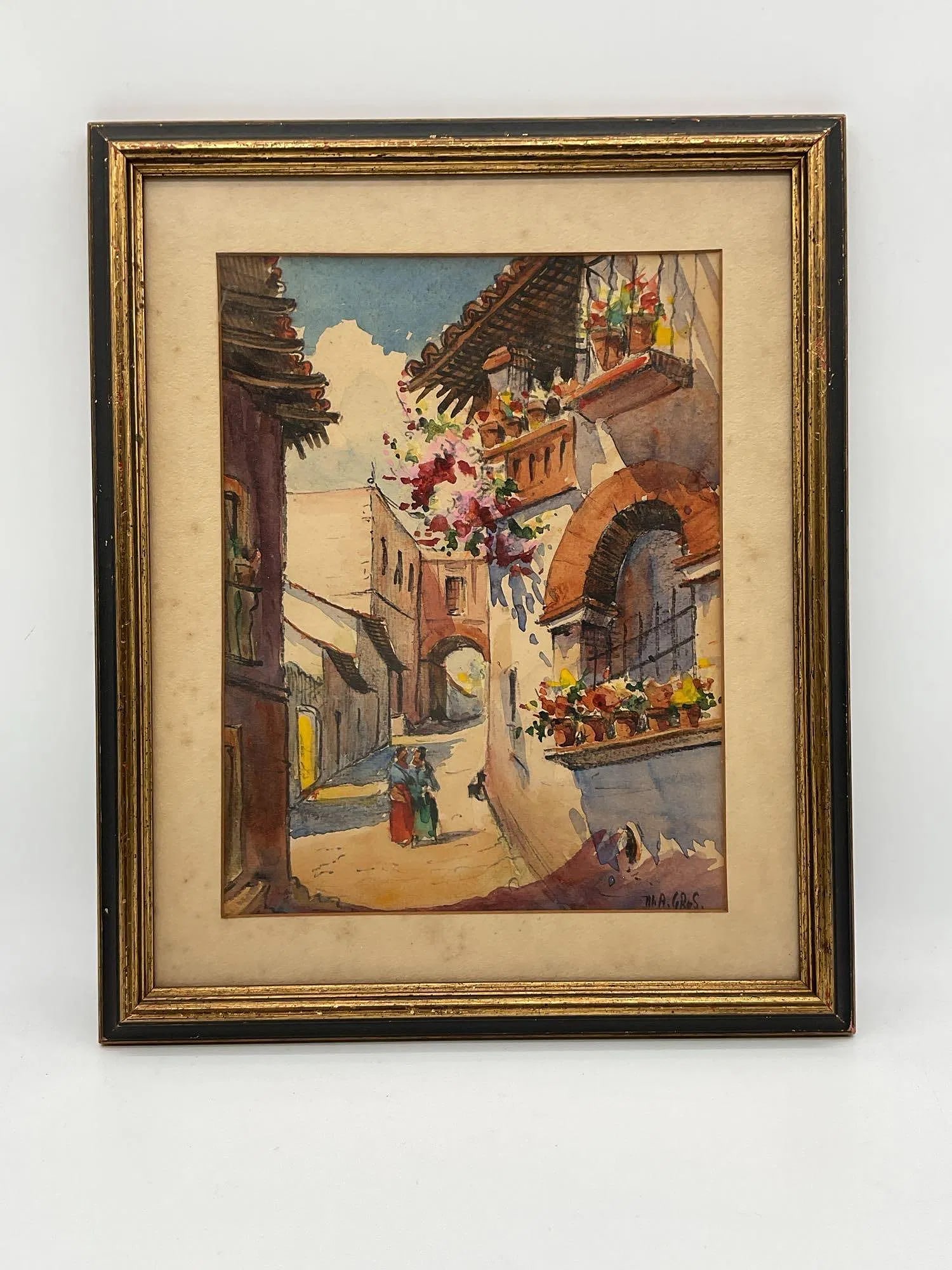 Spanish Street Scene by M.A. Gros Water Color: A charming watercolor depicting a sunlit street in a Spanish village, with traditional architecture, flower-filled balconies, and two women in colorful dresses conversing under a bright sky. Medium:
