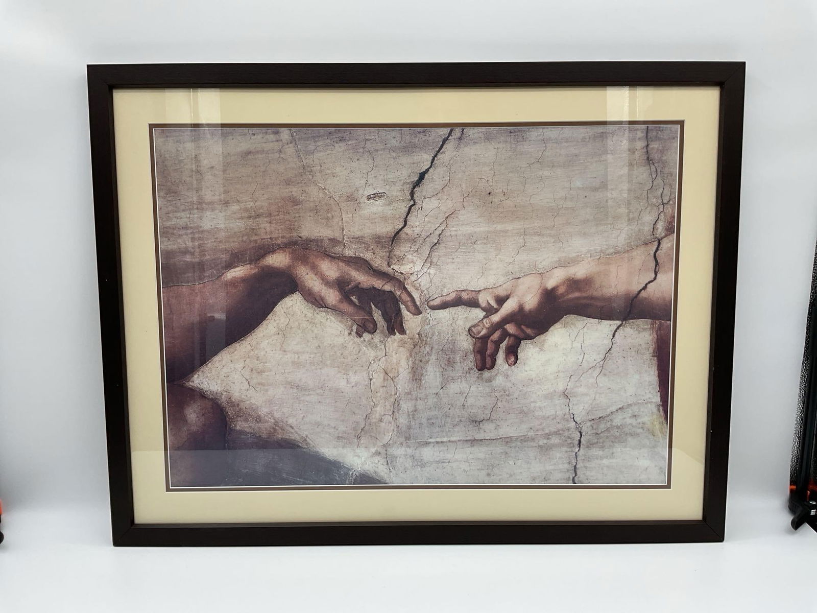 Framed print Creation of Adam detail: Reproduction print of Michelangelo s Creation of Adam, depicting the iconic moment where God s hand reaches out to Adam s. Set in a black frame with beige matte. Dimensions: H26in L33in Medium: P