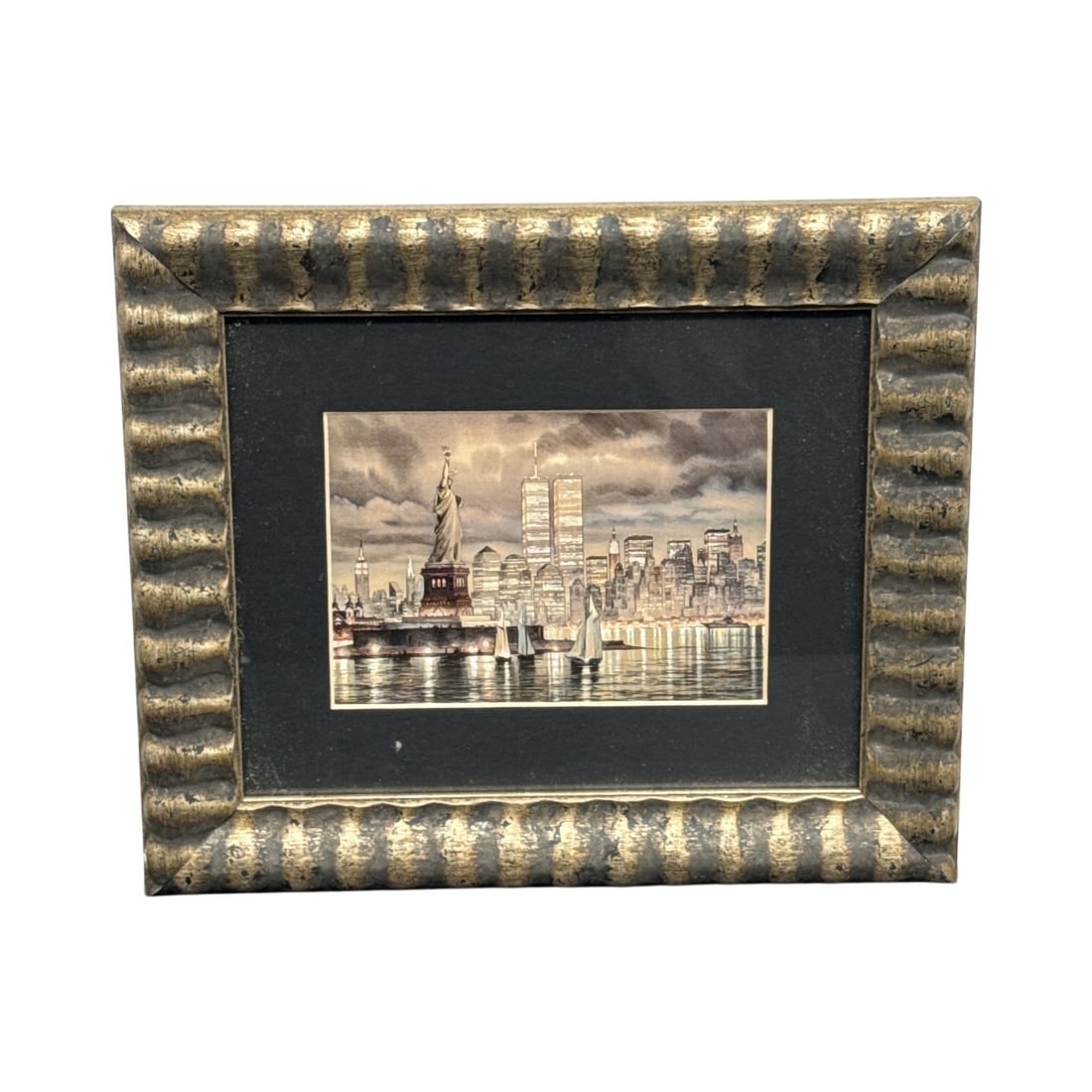 New York City Skyline with Twin Towers Watercolor: Framed print depicting the New York City skyline, featuring the Statue of Liberty, the Twin Towers, and sailboats on the water. The print is matted and set in a decorative gold-toned