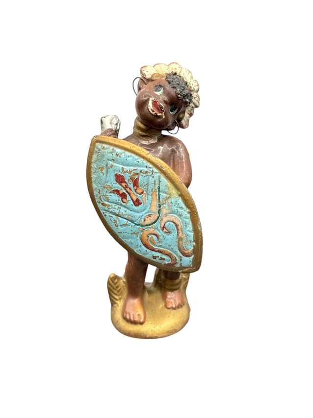 Vintage Mid-Century African Tribal Boy Ceramic Figurine with Shield Hand-Painted: This vintage mid-century ceramic figurine depicts a young tribal boy holding a beautifully decorated shield, rendered in vivid turquoise with red and gold accents. The figure is hand-painted with expr