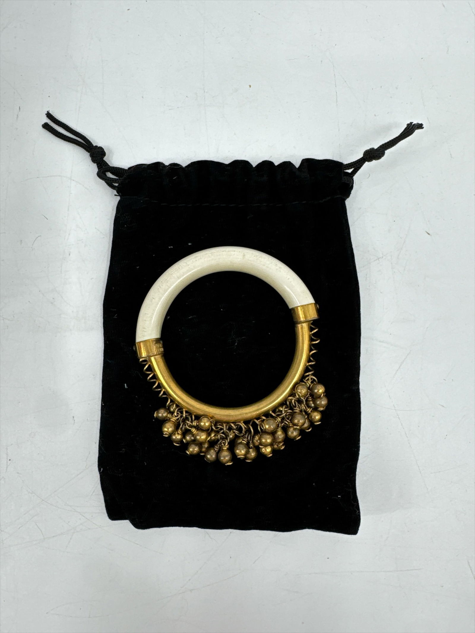 Elegant White and Goldtone Bangle Bracelet with Charms - Valentino: This stunning piece of fashion jewelry features a wide, smooth white or cream-colored band accented with gold-tone caps and dangling charms. The elegant design is reminiscent of high-end designer piec