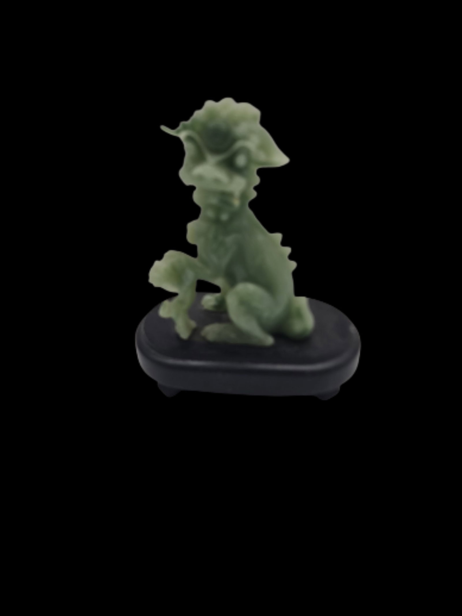 Small Jadeite Foo Dog Figurine: A small guardian lion (Foo Dog) figurine carved in green jadeite-style material, shown in a seated protective pose. The piece includes fine stylized details and is mounted on a simple black display ba