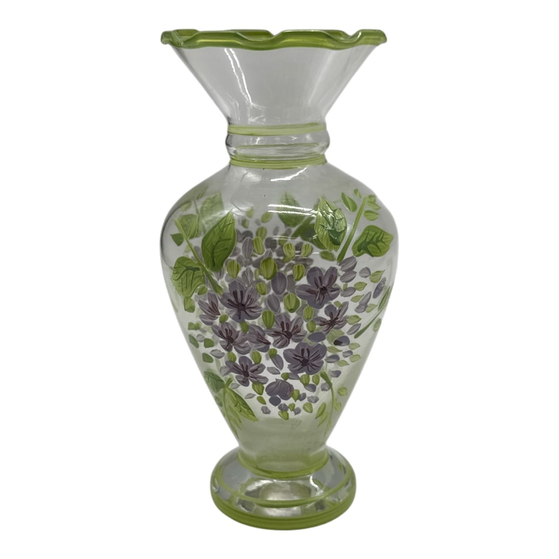 Hand-Painted Glass Vase with Purple Floral Motif: Charming clear glass vase featuring hand-painted purple flower blossoms with green foliage throughout the body. The piece is accented with a softly flared rim and matching green trim, giving it a deli