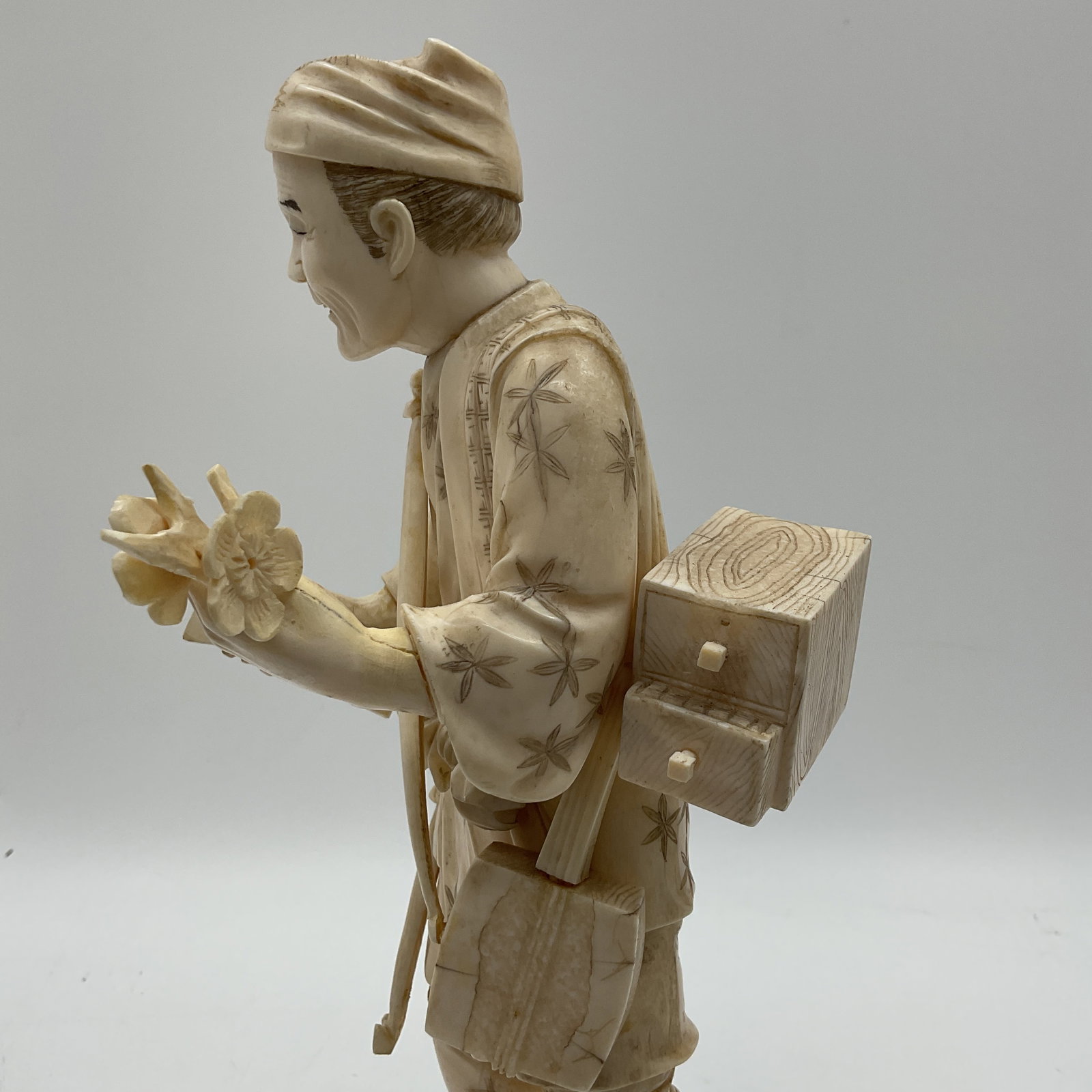 Japanese Carved Bone Figural Okimono: A Japanese carved bone okimono depicting a figure with detailed clothing and accessories, mounted on a wooden base. The carving showcases fine craftsmanship and attention to detail. Height approximate