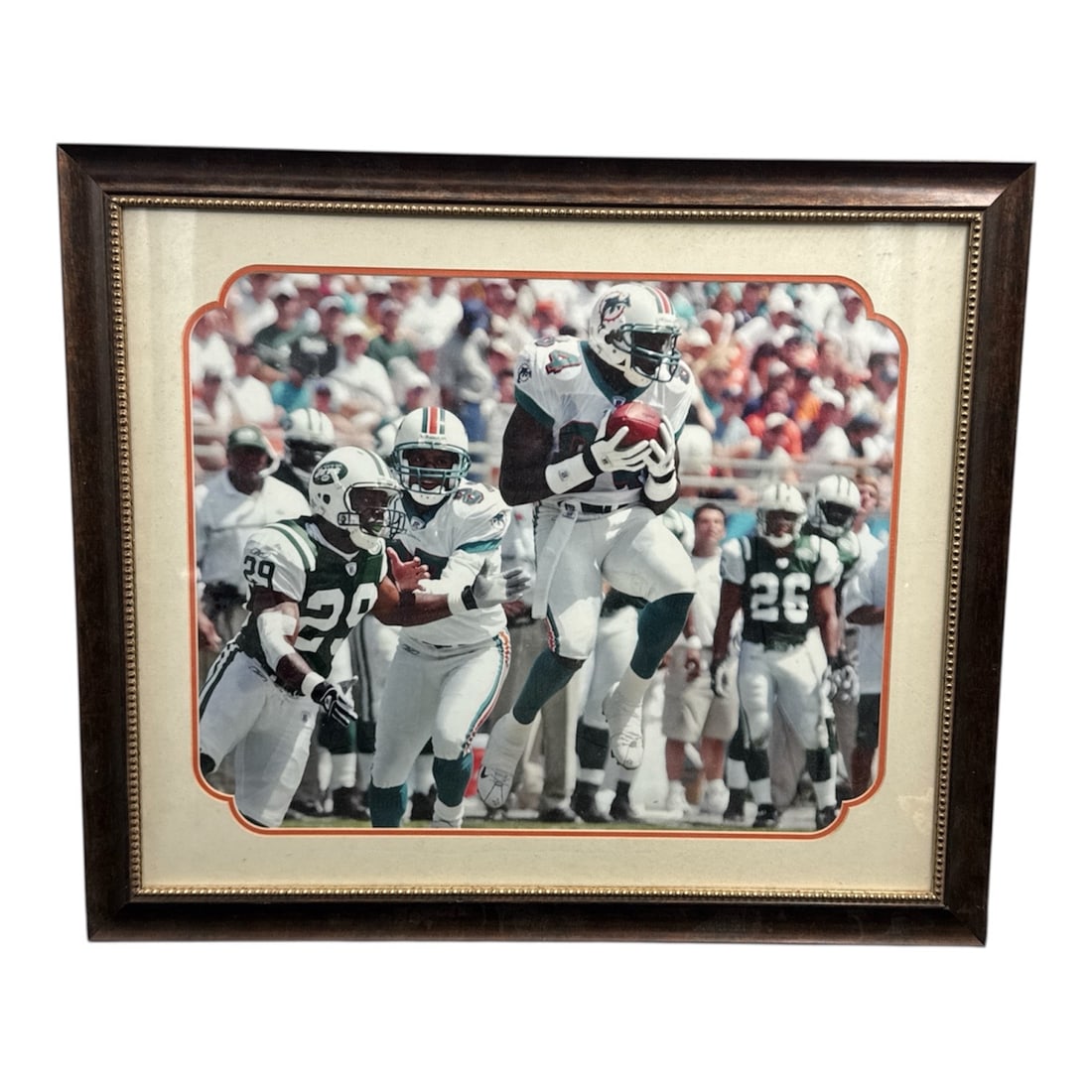 Framed Football Action Photograph Player Leaping Catch Scene: Large framed sports photograph capturing an exciting football moment with a player leaping to make a catch while defenders close in. The dynamic action, stadium crowd backdrop, and classic uniform sty