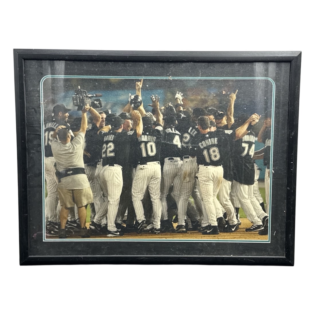 Framed Baseball Team Celebration Photograph Championship Moment: Large framed sports photograph capturing a thrilling baseball team celebration on the field, with players gathered together in victory raising their arms in triumph. The energetic scene conveys the ex