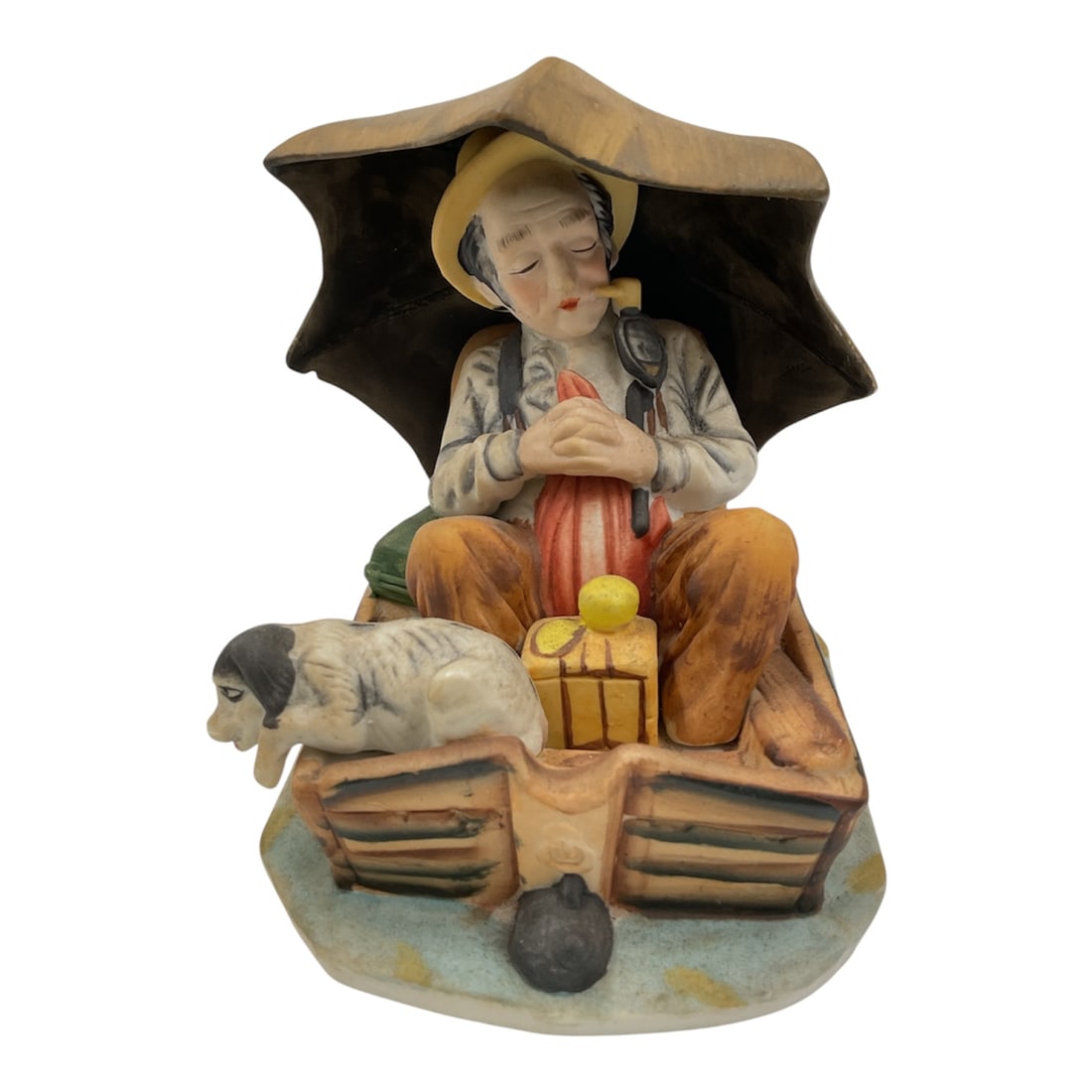 Vintage Norman Rockwell Porcelain Figurine of Man Resting in Boat with Dog: A charming vintage porcelain figurine depicting an Norman Rockwell napping in a small boat beneath an umbrella, accompanied by his dog resting alongside him. The scene is rendered with hand-painted de