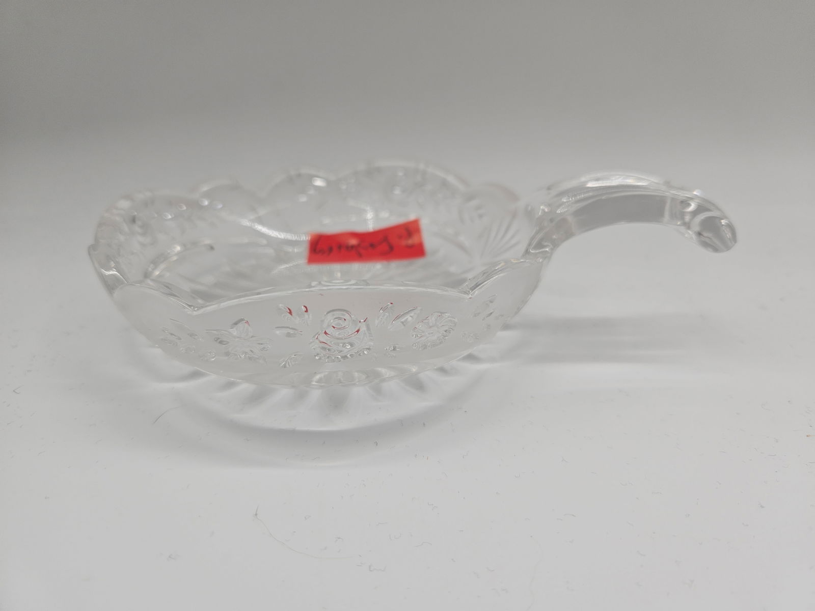 Pressed Glass Bowl with Handle: Clear pressed glass bowl with floral design and attached handle. Dimensions: H: 1in W: 7in L: 5in