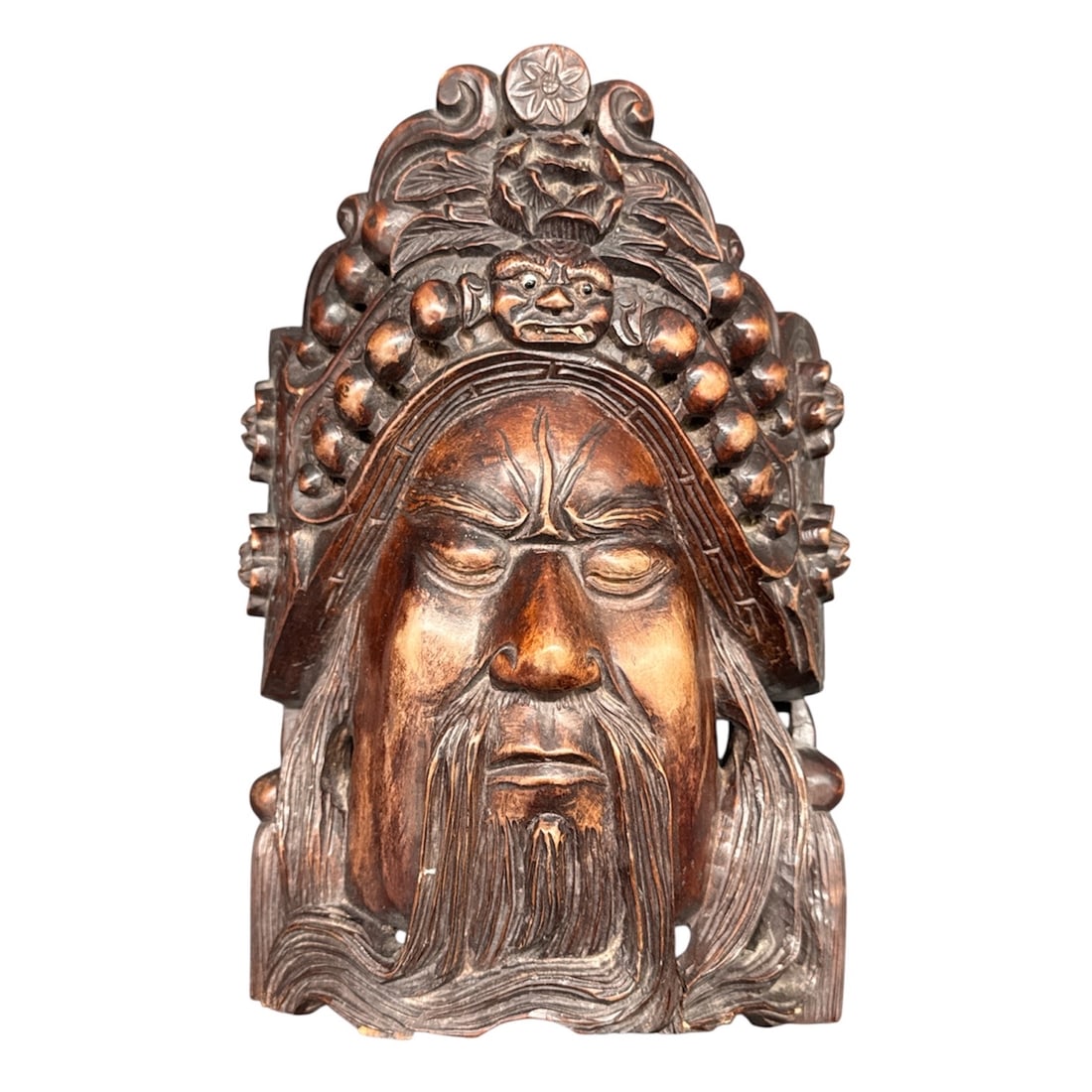 Carved Wood Mask of Bearded Deity or Guardian Figure: Carved wood mask depicting a solemn bearded male figure wearing an elaborate headdress adorned with rounded elements and stylized motifs. The face is rendered with deeply carved features, downcast