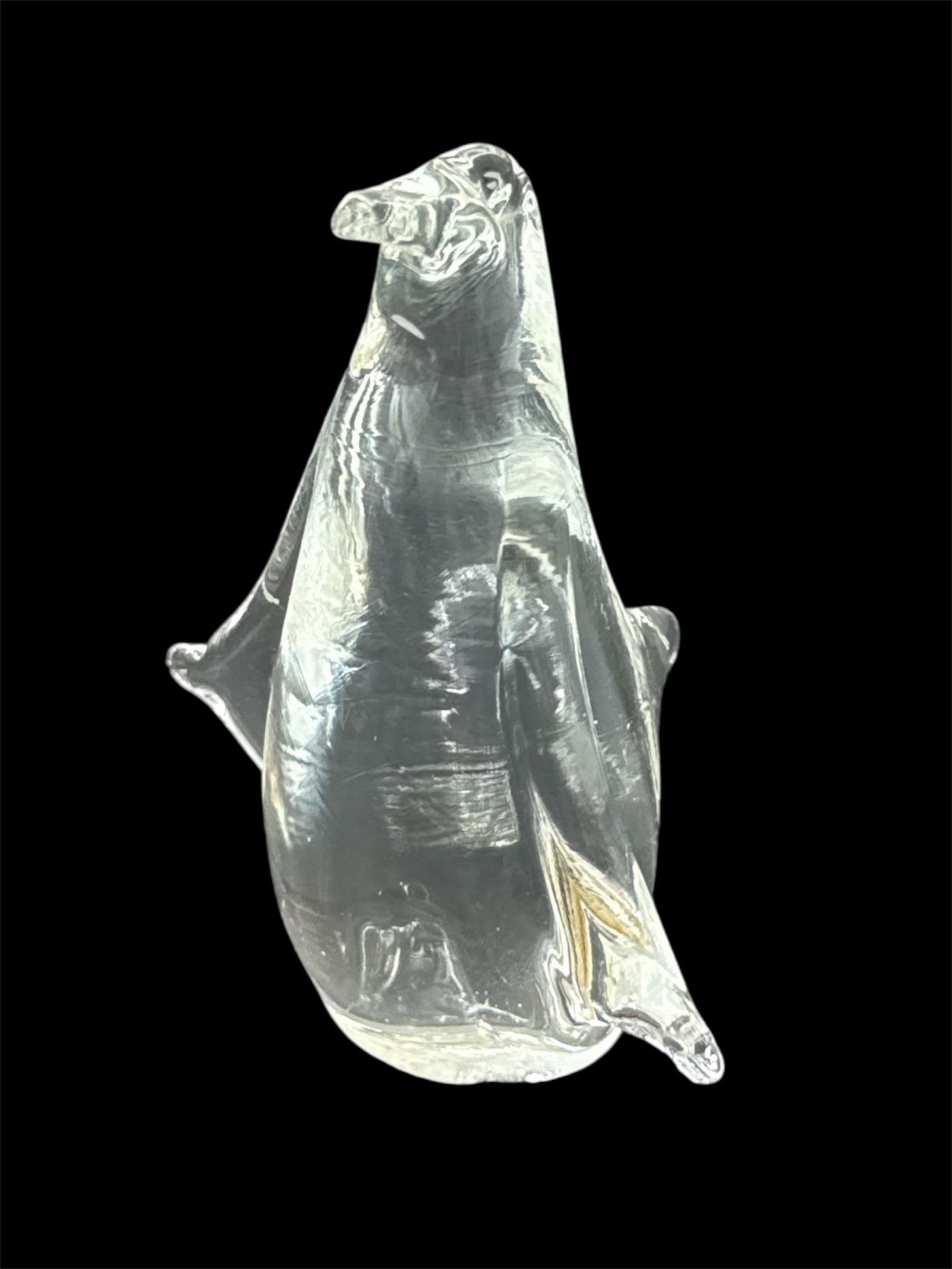 Clear Glass Penguin Figurine: Clear glass figurine depicting a standing penguin with stylized wings and tapered body, rendered in a smooth, minimalist form. The transparent glass surface shows subtle internal reflections and highl
