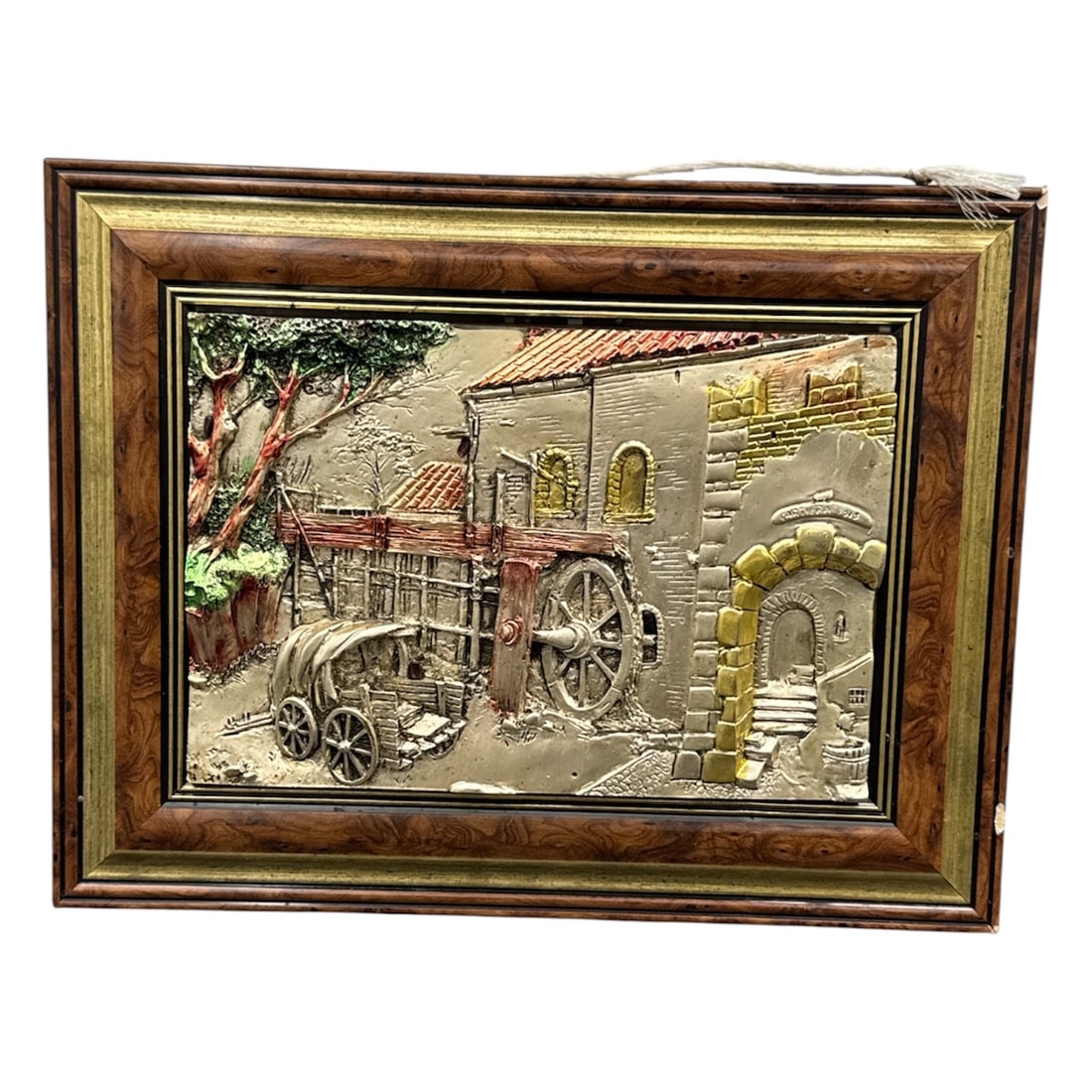 Vintage Framed Three Dimensional Metal Wall Art: A vintage framed three dimensional metal wall art plaque depicting a rustic village scene with architectural elements, a cart, and surrounding landscape rendered in raised relief. The composition feat