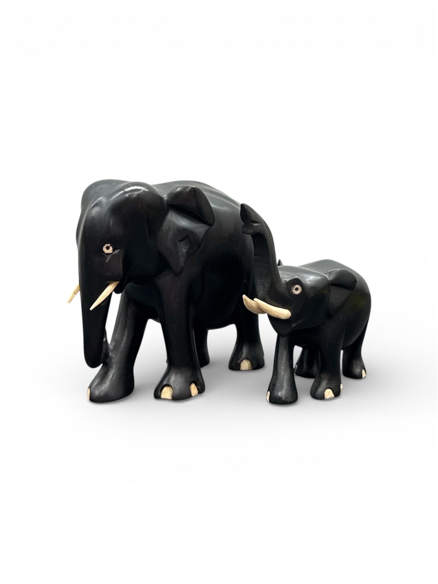 Pair of Carved Black Wood Elephant Figurines: Charming pair of carved black wood elephant figurines depicting an adult and calf. Each figure is carved in rounded form with raised trunks, detailed ears, and inlaid tusk accents. The smooth polished