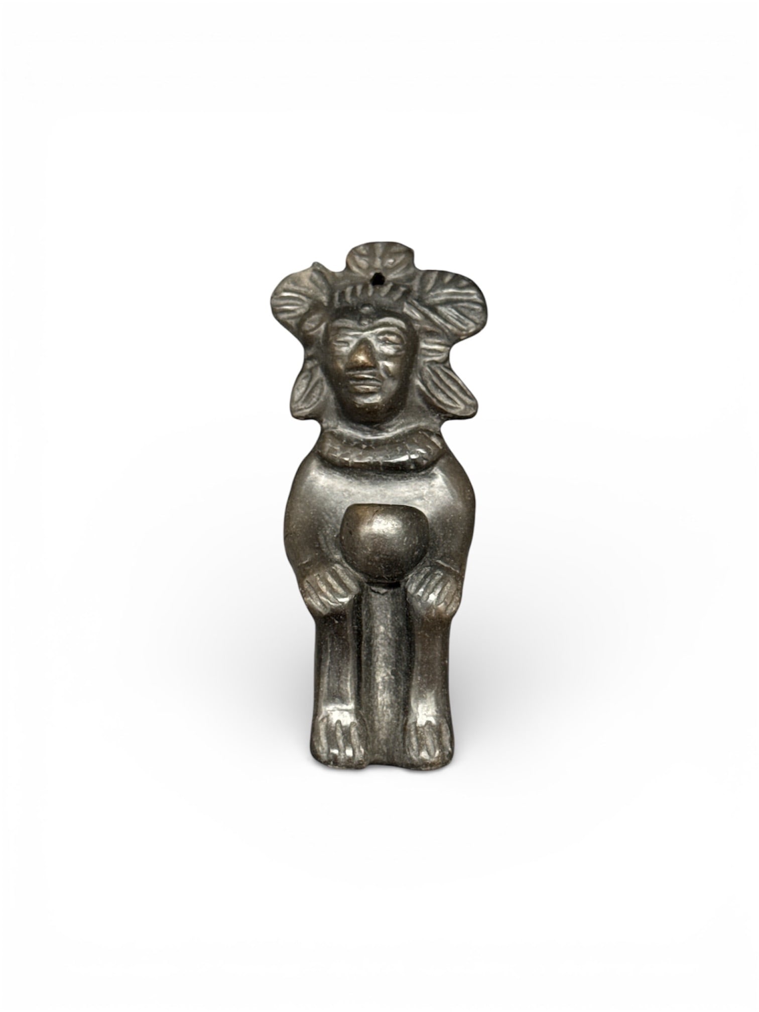 Small Pre Columbian Style Metal Figural Pendant: Small pre Columbian style metal figural pendant depicting a stylized seated figure with pronounced headdress and rounded form. The simplified facial features and symmetrical posture reflect traditiona