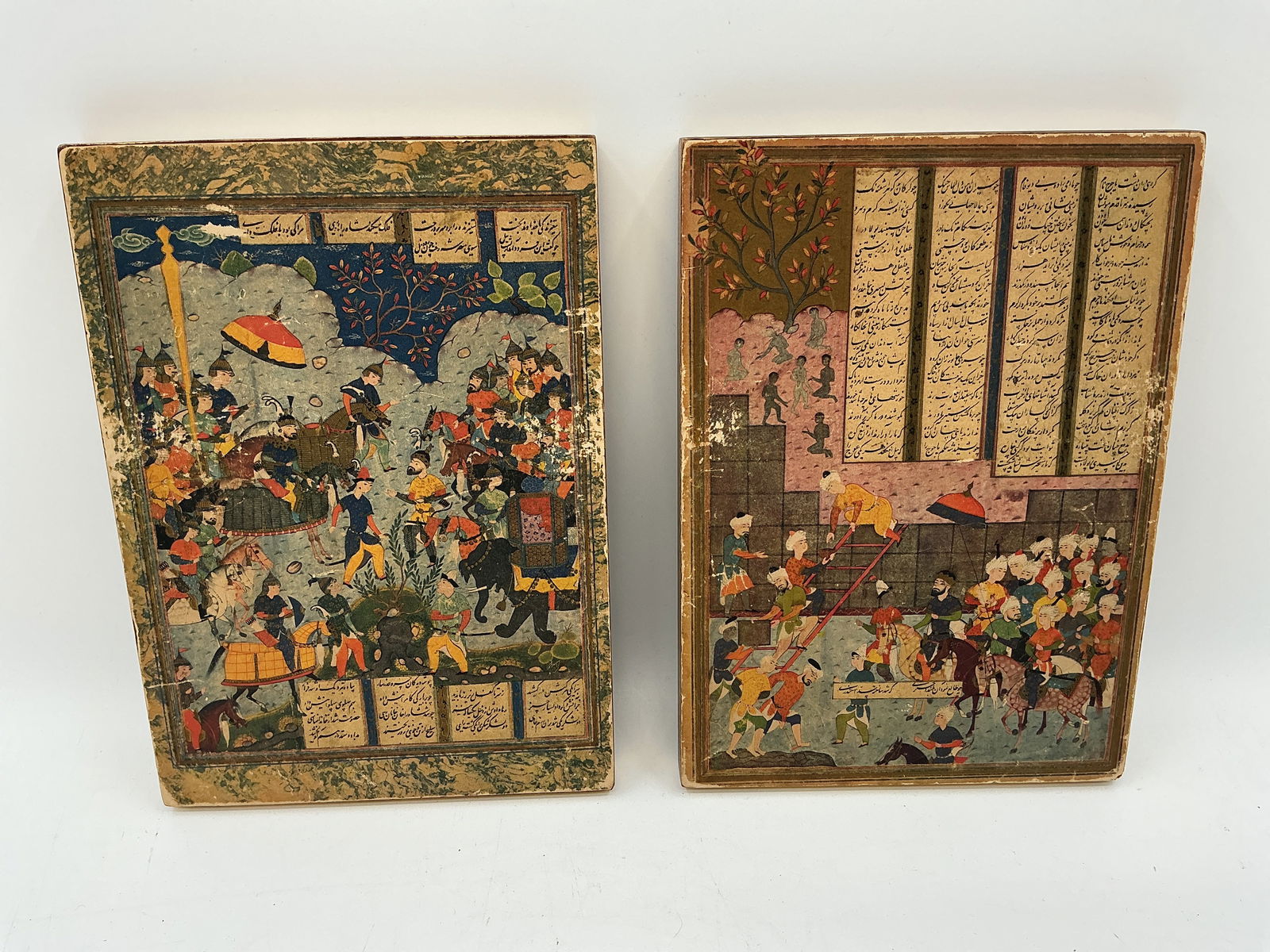 Pair of Persian Miniature Artwork: Two finely detailed Persian miniature artwork, each depicting lively court and battle scenes surrounded by panels of Farsi script. Rich use of color and gold detailing, typical of traditional Persian