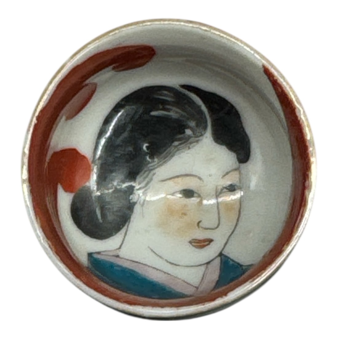 Japanese Porcelain Miniature Bowl with Hand-Painted Geisha Portrait: This miniature Japanese porcelain bowl features a finely hand-painted portrait of a geisha in traditional attire, framed by bold red and black accents along the interior. The expressive face and
