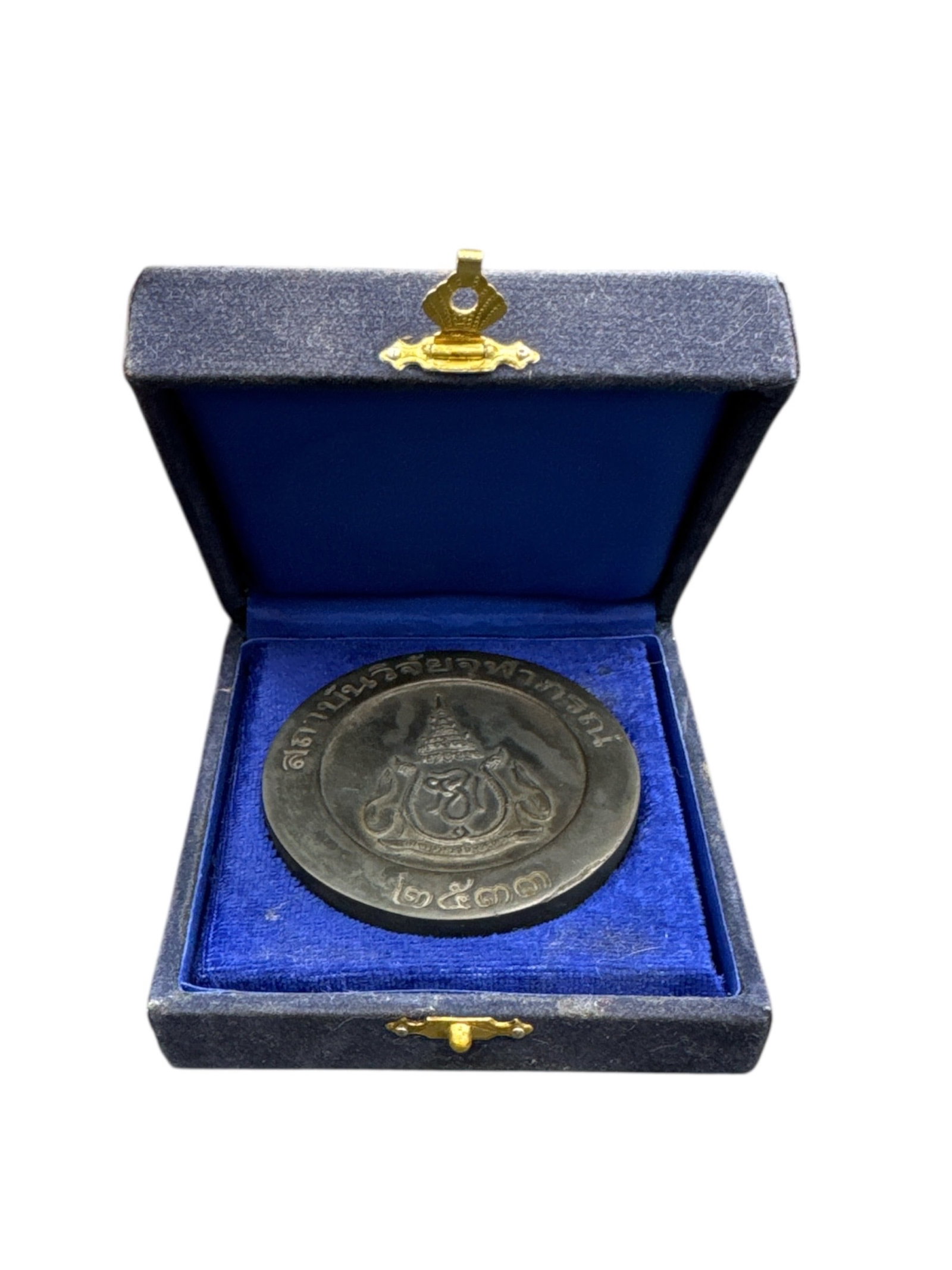 Thai Royal Commemorative Medal, King Bhumibol Adulyadej (Rama IX), 20th Century: Silver-tone Thai royal commemorative medal featuring the crowned royal monogram of King Bhumibol Adulyadej (Rama IX) flanked by stylized naga figures. Thai script inscription surrounds the obverse.