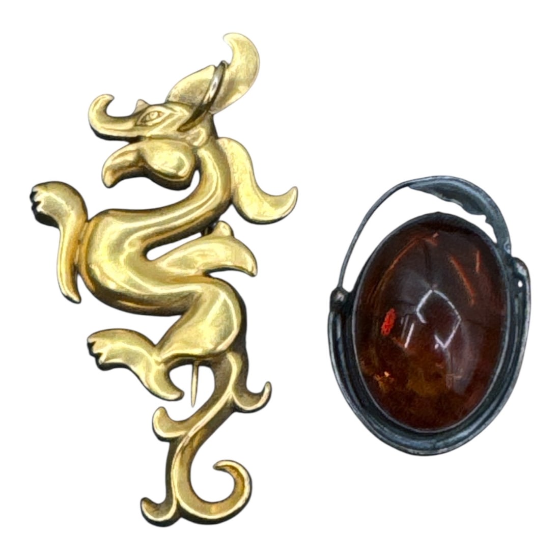 Pair of Vintage Statement Brooches: MMA Gilt Dragon & Amber-Tone Cabochon: This auction features a striking pair of vintage pins that blend mythological flair with classic gemstone aesthetics. Both pieces measure between 2 and 3 inches in length, making them substantial enou