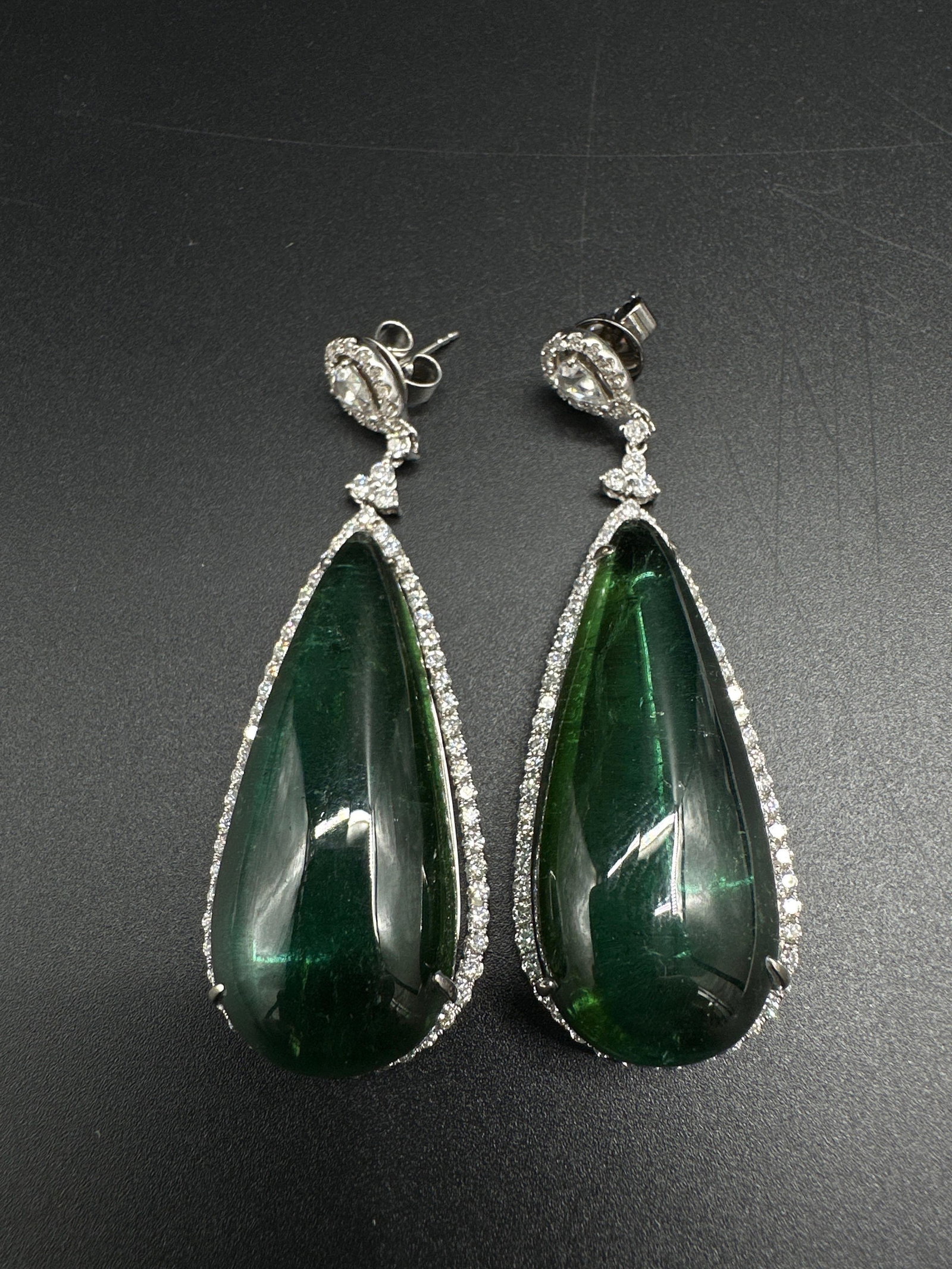 18kt White Gold Diamond & Tourmaline Earrings: Stunning 18kt white gold dangle earrings featuring large pear-shaped green tourmaline stones, accented with round, pear, and rose cut brilliant-cut diamonds in prong settings. Secure post-and-back des