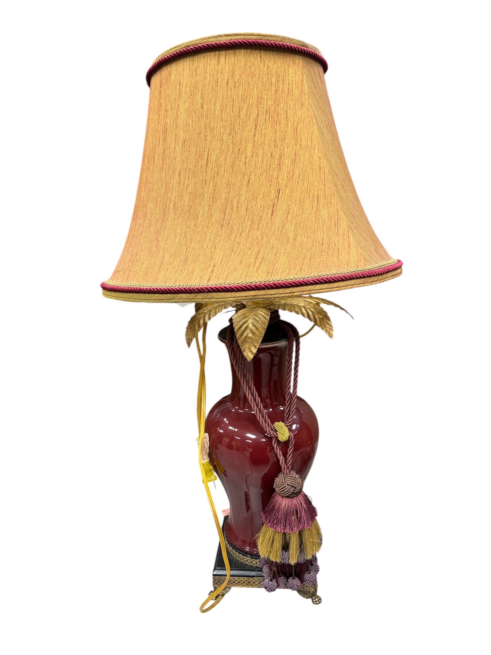 Frederick Cooper Hollywood Regency Oxblood Red Table Lamp with Original Shade: A late 20th century Hollywood Regency style table lamp by Frederick Cooper, featuring a rich oxblood red glazed body accented with decorative tassel and cord motif elements. The sculptural form is com