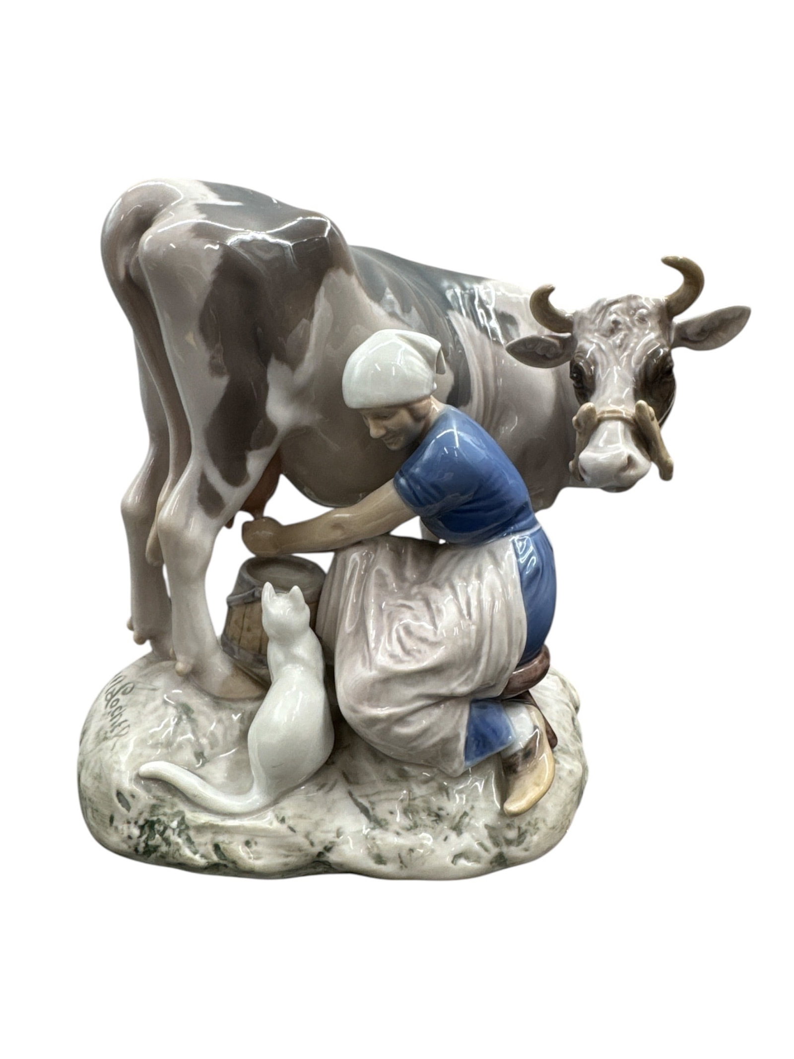 Bing & Grøndahl Porcelain Figurine of Milkmaid with Cow and Cat by Axel Locher: This fine Bing & Grøndahl porcelain figurine depicts a pastoral scene of a milkmaid seated while milking a cow, accompanied by a cat at her feet. Designed by Axel Locher, the composition is