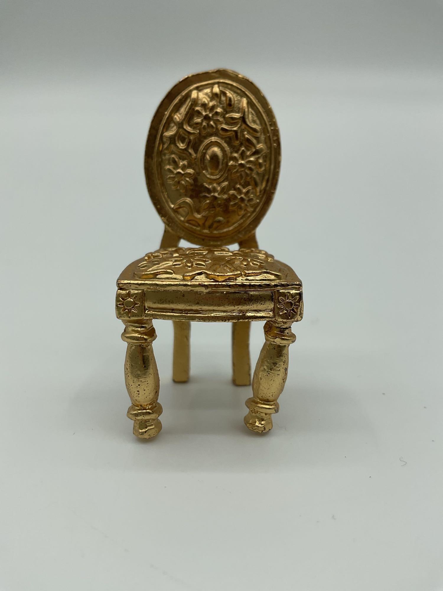 Ornate Miniature Chair Trinket Box: Small gold-tone metal miniature chair with intricate floral and scroll designs on the backrest and seat, likely used as a decorative trinket box or collectible.Dimensions: H2in L1in W1inMedium: Cast