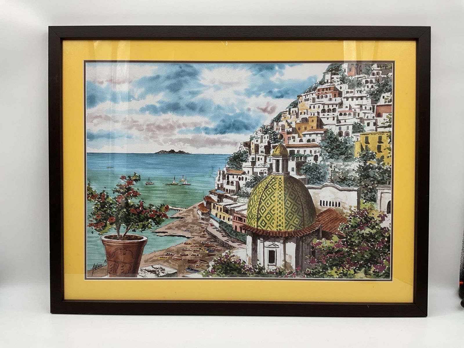 Positano Coastline with Dome: Framed watercolor-style print of Positano, Italy, depicting the iconic dome of the Church of Santa Maria Assunta, a hillside of pastel buildings, and sailboats dotting the turquoise sea. A potted