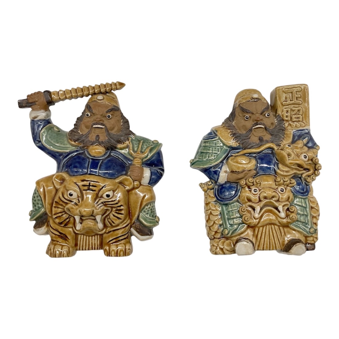 Pair of Chinese Glazed Ceramic Warrior Wall Plaques: Colorful pair of Chinese glazed ceramic warrior plaques depicting traditional guardian figures seated upon stylized mythological beasts. Each figure is rendered in raised relief with vibrant tones of