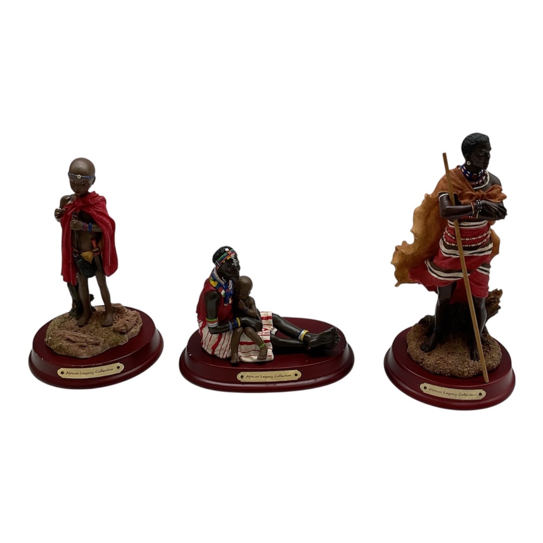 African Legacy Collection Figural Sculptures Group: Group of three African Legacy Collection figural sculptures depicting traditionally dressed figures in detailed and expressive poses. Each figure is mounted on a polished oval base with nameplate, sho