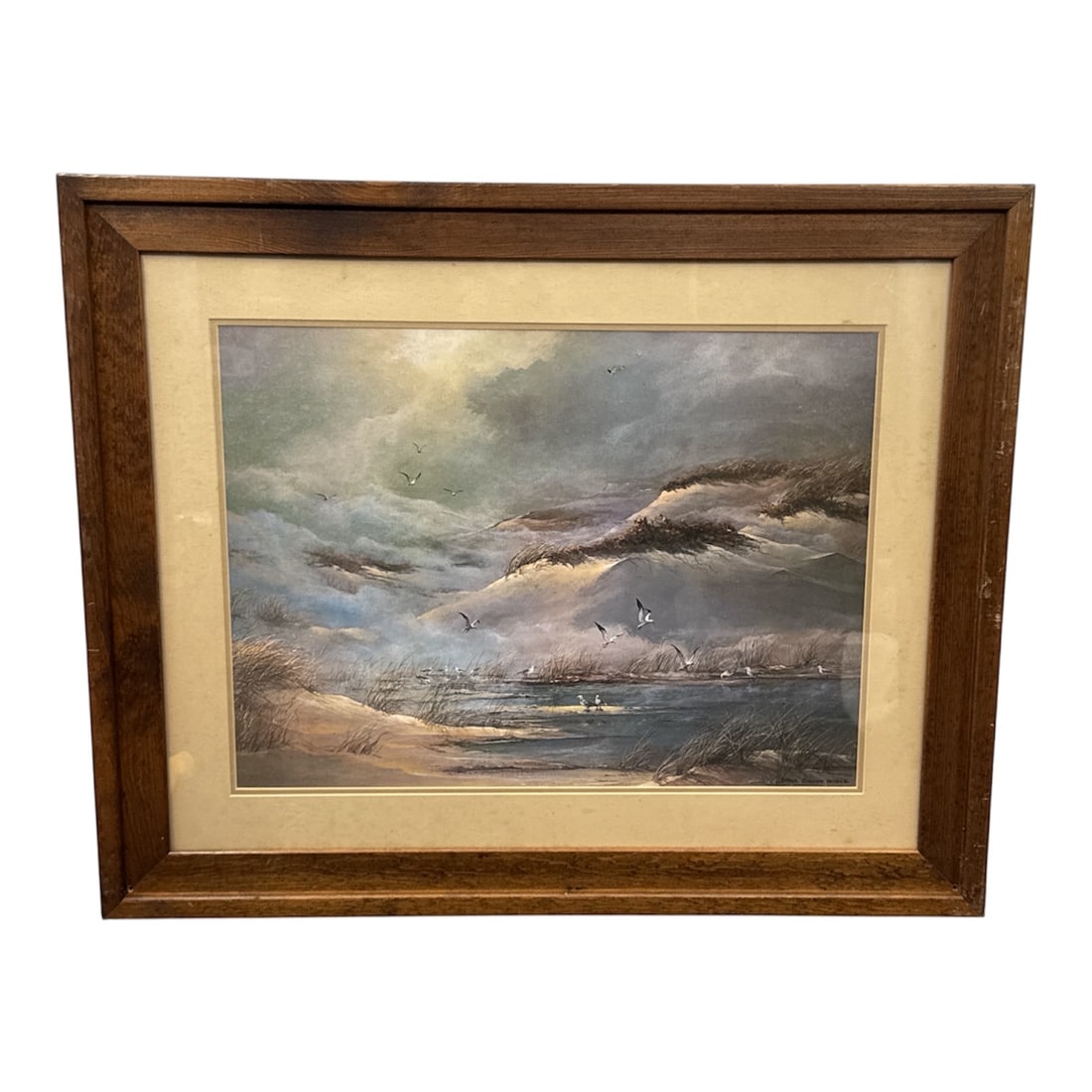 Dana Gibson Noble Coastal Landscape Framed Print: Framed coastal landscape print signed Dana Gibson Noble depicting a dramatic shoreline scene with rolling surf, seabirds in flight, and marsh grasses along the water’s edge. The composition feat
