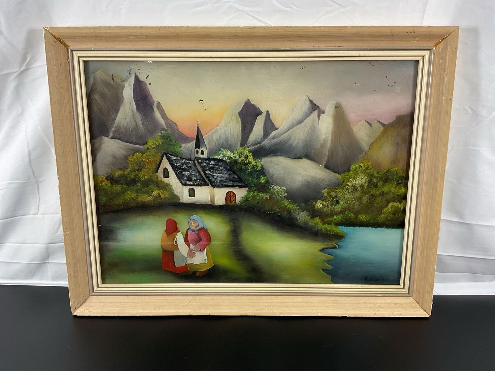"Mountain Village Gathering" by Hornya D (German) Reverse Glass Painting: Description: This charming painting depicts a quaint mountain village scene, featuring a white chapel with a steeple nestled among dramatic, jagged mountains. The foreground showcases two women in