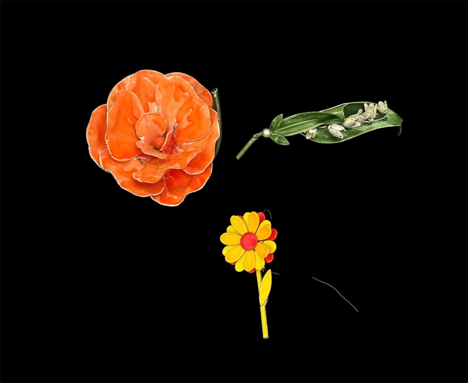 Collection of Vintage Floral Brooches (3): Group of three vintage floral brooches in assorted designs and materials. Includes a large orange molded flower brooch with textured petals, a long green enamel leaf brooch, and a smaller yellow and r
