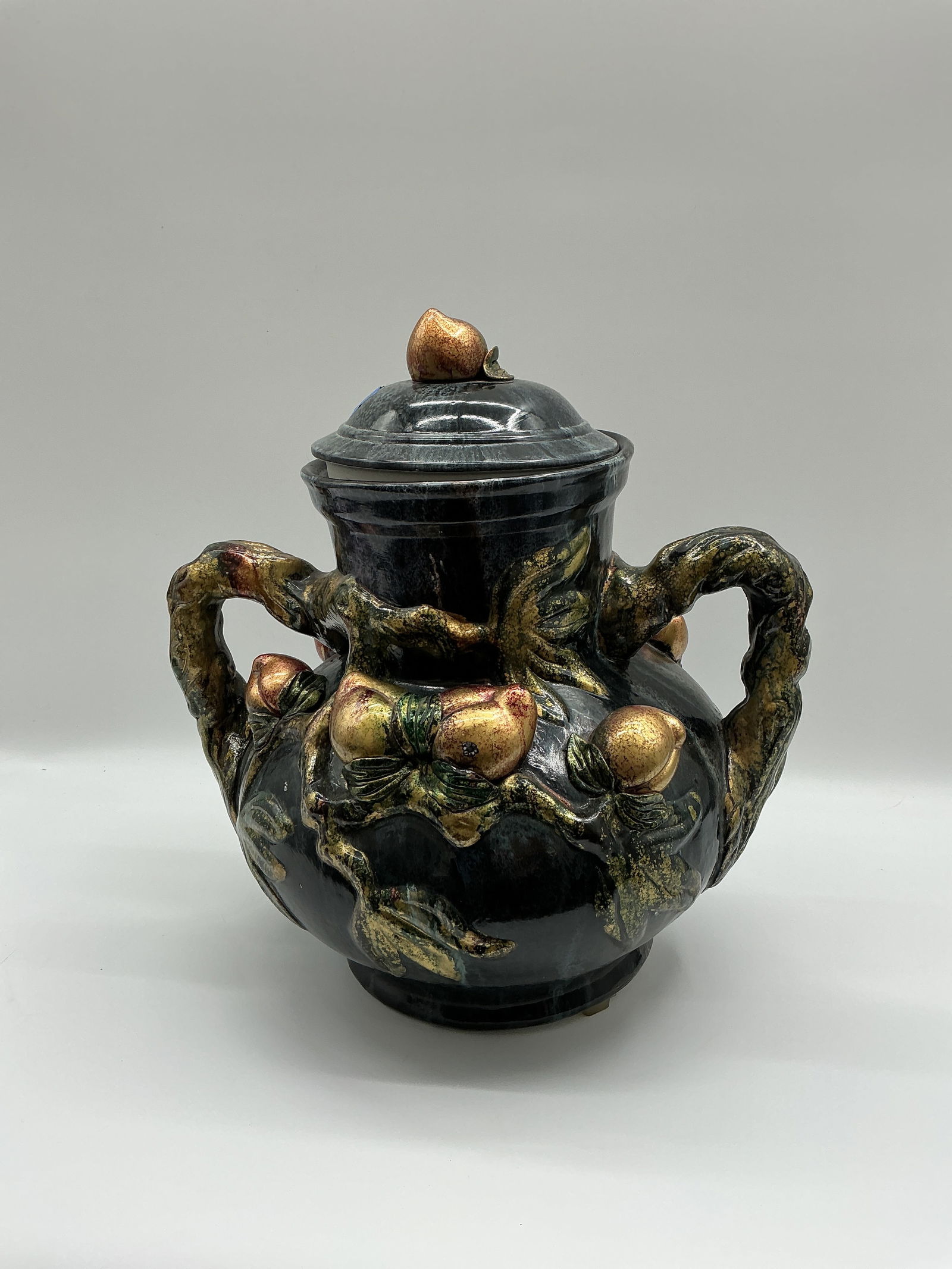 Decorative Lidded Vessel with Floral Design: A decorative lidded vessel featuring a dark body with applied floral and branch details in gold and copper tones. The vessel has two handles and a removable lid. Dimensions approximately 14 inches