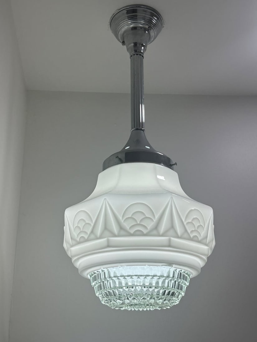 Art Deco Style Frosted Glass Pendant Ceiling Light with Chrome Hardware: This ceiling-mounted pendant light features a sculptural frosted glass shade with stepped and geometric detailing inspired by classic Art Deco design. The fixture is suspended from a chrome-finished c