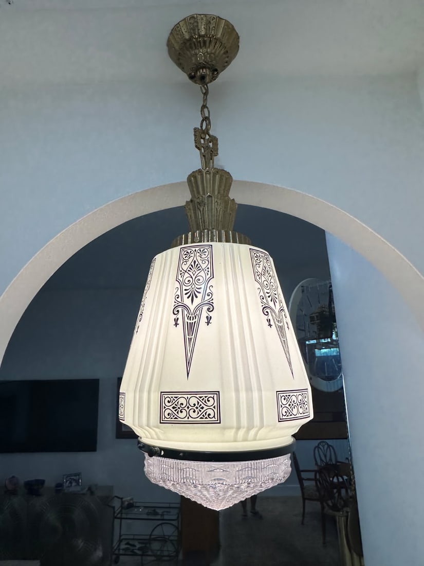 Art Deco Style Frosted Glass Pendant Ceiling Light with Ornate Metal Hardware: This ceiling-mounted pendant light features a frosted molded glass shade decorated with geometric and stylized motifs characteristic of Art Deco design. The shade is paired with ornate metal hardware