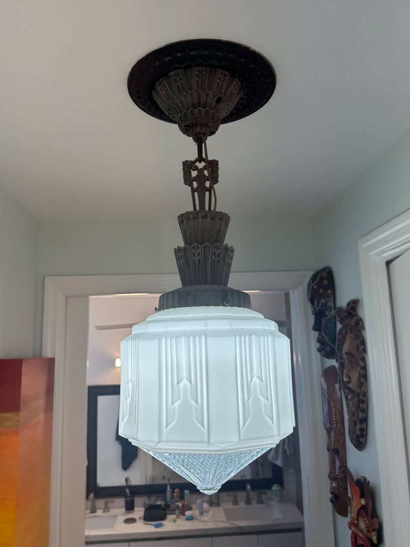 Art Deco Style Frosted Glass Pendant Ceiling Light with Ornate Metal Hardware: This ceiling-mounted pendant light features a stepped frosted glass shade with bold geometric panels inspired by classic Art Deco design. The fixture is paired with ornate metal hardware, including a