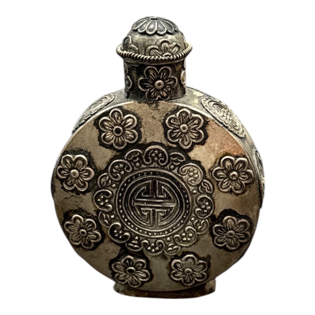 Antique Chinese Silver-Tone Snuff Bottle with Floral Motifs and Spoon Stopper: Decorative Chinese snuff bottle featuring a rounded form richly adorned with raised floral motifs and a central longevity symbol medallion. Finished in a silver-tone metal with detailed